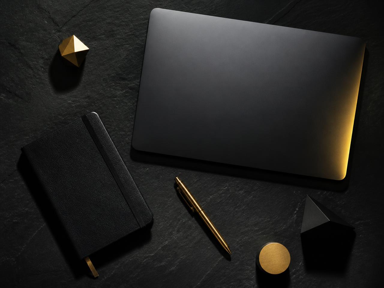 Laptop, gold pen and leather notebook arranged on black slate